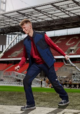 Man in werkkleding trekt een palletwagen door een voetbalstadion.